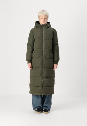 Pikk oliiviroheline voodriga parka kapuutsiga, millel on ees lukuga kinnitamine, suured taskud ja kergelt läikiv pind. Kanna laiade teksade peal.