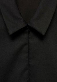 Czarna koszula z kołnierzykiem w kształcie szpicu, gładką teksturą i centralnym zapięciem na guzik. Materiał ma subtelny połysk i dopasowany krój.