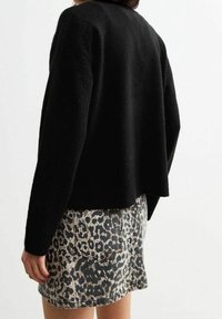 Schwarzer Wollmischpullover mit lockerer Passform, kombiniert mit einem grauen Jeansrock im Leopardenmuster, der über Gesäßtaschen und einen fransigen Saum verfügt.