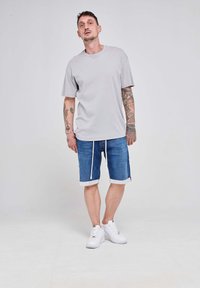 Siva bombažna majica s kratkimi rokavi, v kombinaciji z modrimi denim kratkimi hlačami z vrvico in zavihkom, obuta v bele superge.