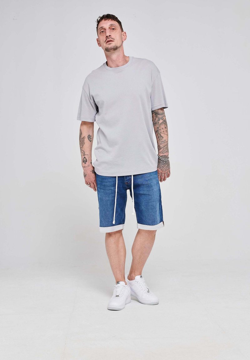 Siva bombažna majica s kratkimi rokavi, v kombinaciji z modrimi denim kratkimi hlačami z vrvico in zavihkom, obuta v bele superge.