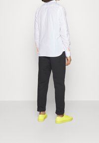 Biała koszula z długim rękawem z pomarańczowymi akcentami, w zestawieniu z ciemnoszarymi spodniami i jasnymi żółtymi trampkami. Gładki materiał i luźny fason.