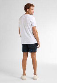 Biała koszulka z krótkim rękawem z okrągłym dekoltem, zestawiona z ciemnymi szortami w wzory z niebieskimi kwiatami i beżowymi sneakersami.