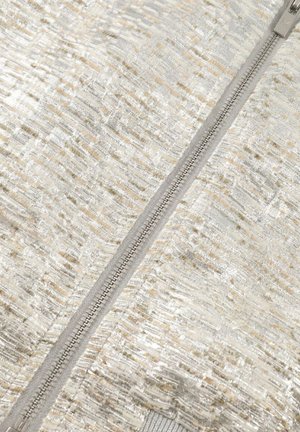 Close-up van een beige, gestructureerde stof met zilveren accenten en een centrale zilveren ritssluiting.