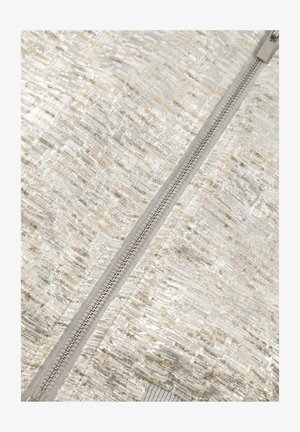 Close-up van een beige, gestructureerde stof met zilveren accenten en een centrale zilveren ritssluiting.