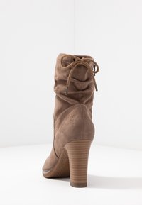 Stivale ankle in suede marrone con design sbagagliato, dettaglio lacciato nella parte superiore e tacco impilato testurizzato. Parte superiore liscia e punta rotonda.
