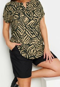 Top a maniche corte caratterizzato da un motivo astratto beige e nero, con una vestibilità rilassata e un leggero scollo rotondo; abbinato a shorts neri.