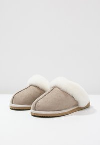 Pantofole beige in morbido camoscio con un risvolto in pelliccia sintetica bianca. Presentano una punta arrotondata e una suola in gomma leggera per il massimo comfort.