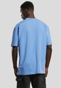 Tricou din bumbac de culoare albastră deschisă, cu mâneci scurte și croi lejer, având gât rotund și textură fină. Vedere din spate.