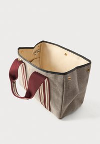 Ορθογώνια μπεζ τσάντα tote από καμβά με μαύρες άκρες και πλατιές μπορντό λαβές, με κρέμες ρίγες, εμφανίζεται ανοιχτή με ορατό εσωτερικό ύφασμα.