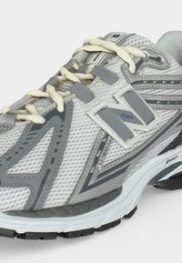 Λευκό και γκρι αθλητικό παπούτσι New Balance για τρέξιμο με επάνω μέρος από δίχτυ, μαλακή σόλα και μπεζ κορδόνια δεμένα φιόγκο.
