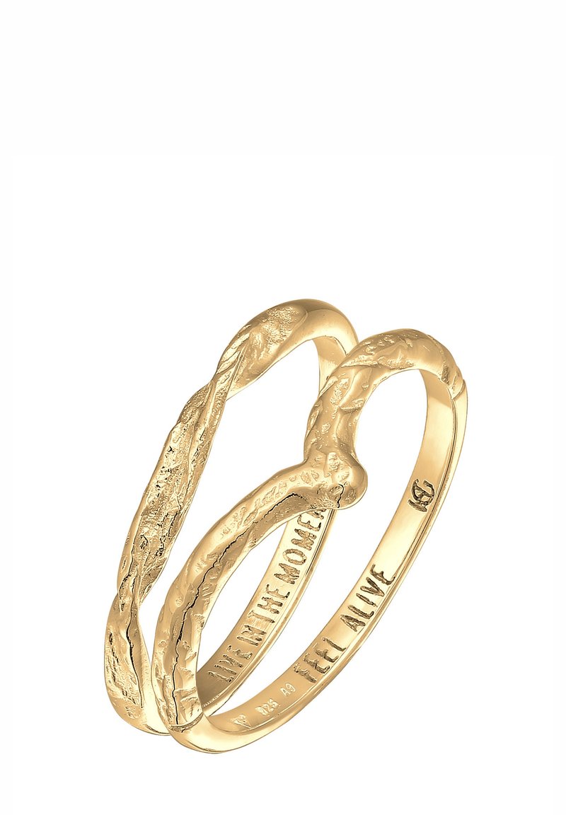 Zlaté krúžky s prepletaným dizajnom majú textúrovaný povrch, na ktorom sú vyryté frázy „ŽI V PRÍTOMNOSTI“ a „CÍŤ SA ŽIVO“.