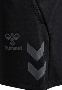 Svarta idrottsshorts med en zipficka, texturerat tyg och grå logotyp med chevrondetaljer på sidan.