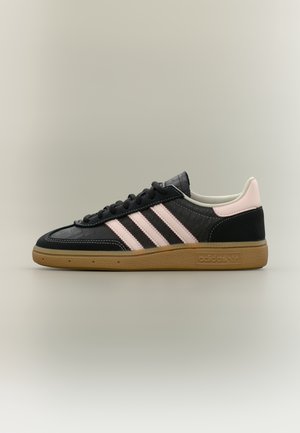 Czarny sneaker adidas z różowymi paskami, jasnoróżową patką na pięcie i gumową podeszwą na neutralnym tle, widok z boku.