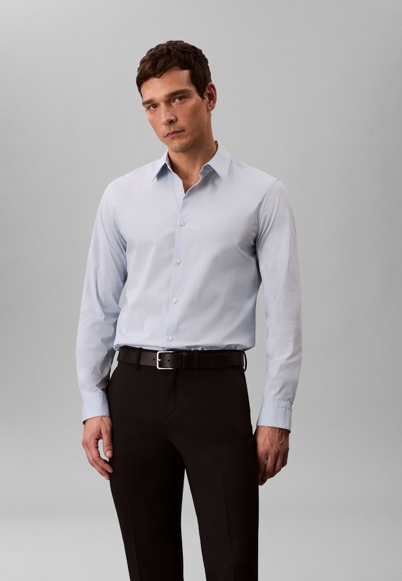 Hele sinine pikakäisega kleit-särk terava kraega, nööpidega ees ja peene kaubamärgiga. Sobitatud mustade pükste ja musta vööga.