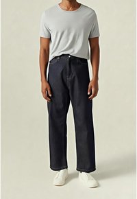 Jasnoszary bawełniany T-shirt w połączeniu z ciemnoniebieskimi jeansami o szerokich nogawkach. Jeansy mają klasyczny fason z pięcioma kieszeniami i jasnym przeszyciem.