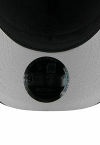 Schwarz-weiße New Era 9FORTY M-CROWN Cap aus strukturiertem Stoff, mit verstellbarem Riemen und einem runden Etikett, das Markendetails zeigt.