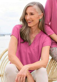 Rosa V-Ausschnitt-T-Shirt aus weichem Stoff, vor einem hellen Hintergrund. Kurzärmlig, mit lockerem Schnitt und dezenter Textur.