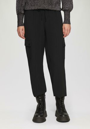Schwarze Cargo-Hosen mit Seitentaschen, elastischem Bund und lockerer Passform. Kombiniert mit schwarzen Schnürstiefeln für einen stimmigen Look.