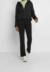 Svart puffjacka med horisontella sömmar, dragkedja fram och huva, i kombination med svarta ribbade utsvängda byxor och ljusfärgade sneakers.