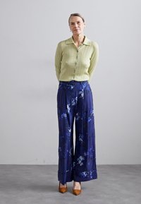 Light green ribbed cardigan with buttons layered over navy floral wide-leg trousers featuring blue and white patterns; brown heels.