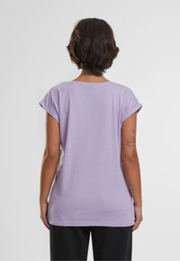 Lilla kortærmet t-shirt lavet af blødt stof, med en afslappet pasform og oprullede ærmer, set bagfra. Enkel design uden mønstre.