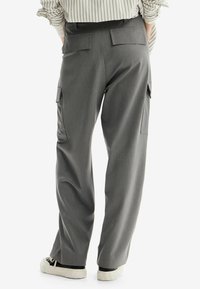 Pantaloni cargo grigi con vestibilità dritta, caratterizzati da due tasche posteriori e tasche laterali. Il tessuto è liscio con una sottile textura. Sneakers bianche visibili.