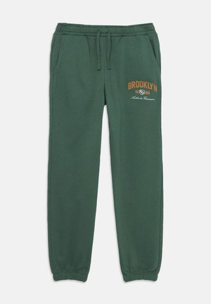 Grüne Baumwoll-Sweatpants mit elastischem Bund und Bündchen, mit braunem "BROOKLYN 1986" Grafik auf der Vorderseite und seitlichen Taschen.