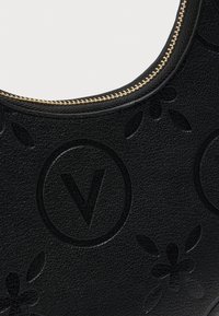 Bolso de mano de cuero negro con diseños en relieve de flores y logotipos, con una cremallera dorada en el borde superior para cierre.