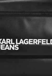 Borsa nera strutturata con chiusura a zip; presenta un grande testo bianco "KARL LAGERFELD JEANS" sulla parte anteriore.