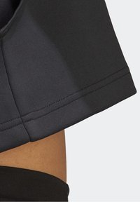 Gros plan d'un ourlet en tissu noir sur un vêtement au-dessus de la peau nue avec couture visible et détails de coutures.