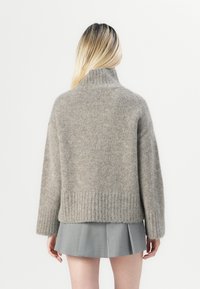 Gray knit sweater with a high collar, ribbed hem, and long sleeves; worn over a gray pleated skirt. Soft, textured material.