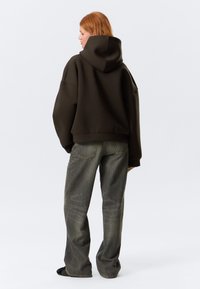 Sweatshirt oversized castanho com um capuz grande, combinado com jeans de ganga cinza flare com bolsos traseiros e detalhes de textura subtil.