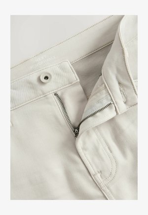 Světle béžové slim-fit kalhoty vyrobené z flexibilního materiálu; obsahují zip, zapínání na knoflík a prošívané detaily v oblasti kapsy.