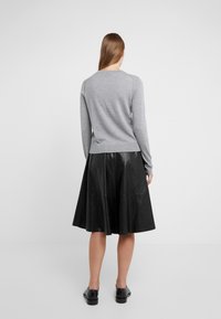 Šedý svetr vyrobený z měkké tkaniny s dlouhými rukávy, doplněný černou koženou midi sukni s rozšířeným střihem a švy.