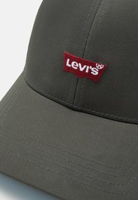 Gorra gris de tela texturizada con visera curvada. Un logo rojo bordado de Levi's se exhibe de manera prominente en la parte frontal.