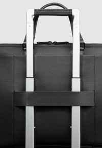 Zwarte stoffen reistas met een zilverkleurige uitschuifbare handgreep. De handgreep heeft een gevoerde bovenkant en een zwarte band voor stabiliteit.