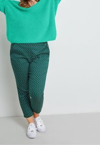 Turkusowy puszysty sweter o luźnym kroju w połączeniu z ciemnozielonymi spodniami z geometrycznym białym wzorem oraz białymi sneakersami.