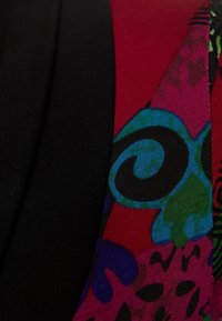 Gros plan sur un tissu noir à côté d'un tissu à motifs vibrants avec des formes abstraites en spirale et florales en rouge, bleu, vert, violet et noir.