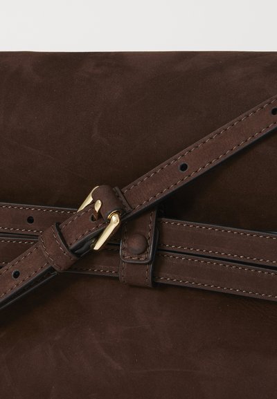 Bolso de ante marrón con un diseño plano. Presenta una superficie texturizada, herrajes en tono dorado y una correa de cuero con múltiples agujeros de ajuste.