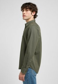 Olijfgroene longsleeve shirt met een button-down kraag, voorzien van een borstzak en zijsplitten aan de zoom voor een relaxte pasvorm.