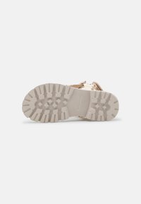 Jasno beżowe obuwie z teksturowaną kremową gumową podeszwą. Charakteryzuje się rugged wzorem bieżnika i brązowymi sznurowadłami, zaprojektowane z myślą o trwałości.