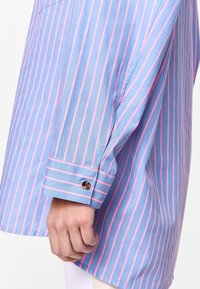 Long-sleeve shirt in light blue fabric with pink vertical stripes. Features buttoned cuff and a relaxed fit silhouette.