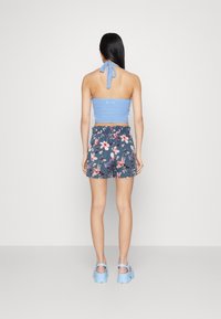 Modrý háčkovaný halter top, tmavé šortky s květinovým vzorem a světle modré chunky sandály. Hladká textura, přiléhavý design a ležérní styl.