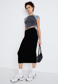 Un crop top gris et bleu, une jupe midi noire en tricot ajustée, des baskets blanches avec des accents navy, et un petit sac à main noir.