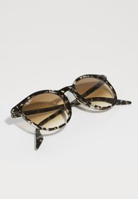Gafas de sol con lente de degradado marrón y montura de plástico con patrón de carey negro, que presentan lentes redondos audaces y brazos gruesos.