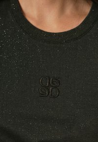 Donkergroen t-shirt met een ronde halslijn, met een glinsterende textuur en een geborduurd logo in de hoek onderaan.