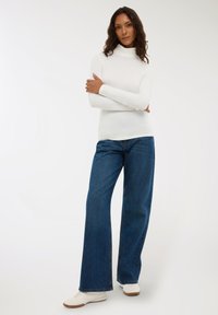 Maglione a collo alto bianco a maniche lunghe abbinato a jeans di denim blu a vita alta e gamba larga, con sneakers bianche. Tessuto morbido, vestibilità casual.