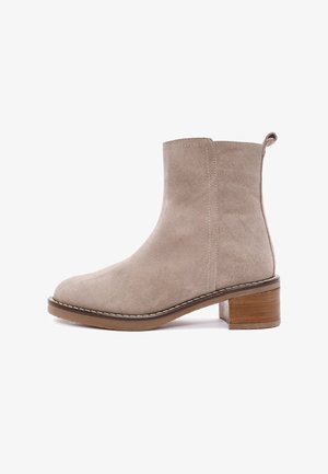 Bottine en suédine beige avec un bout arrondi, un talon bloc en bois de 4 cm et un discret surpiquage le long de la semelle. Tirant à l'arrière pour faciliter l'enfilage.