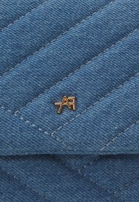 Modrý prošívaný materiál s diagonálními švy a malým zlatým kovovým logem ve tvaru písmen "AA".